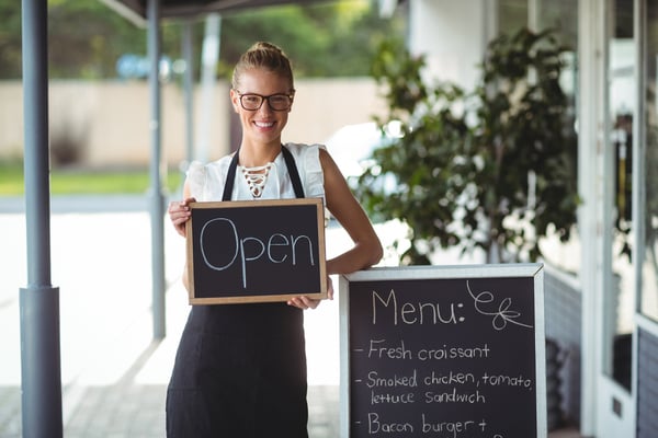 Portrait of waitress standing with chalkboard and menu outside the cafe