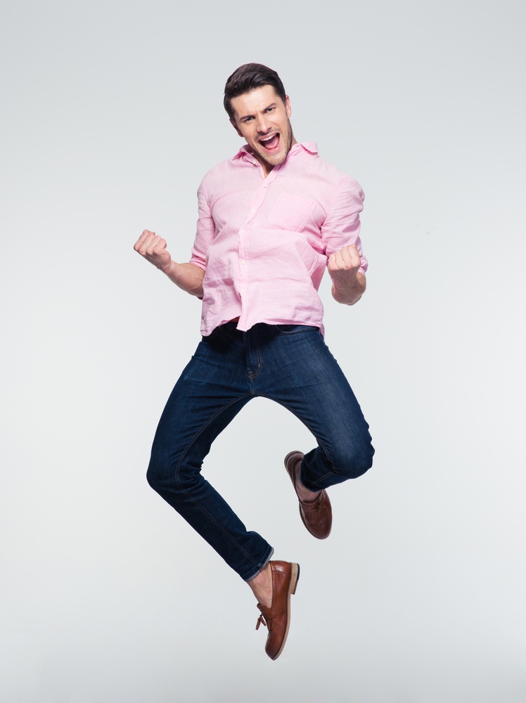 Businessman celebrating his success and jumping over gray background. Looking at camera